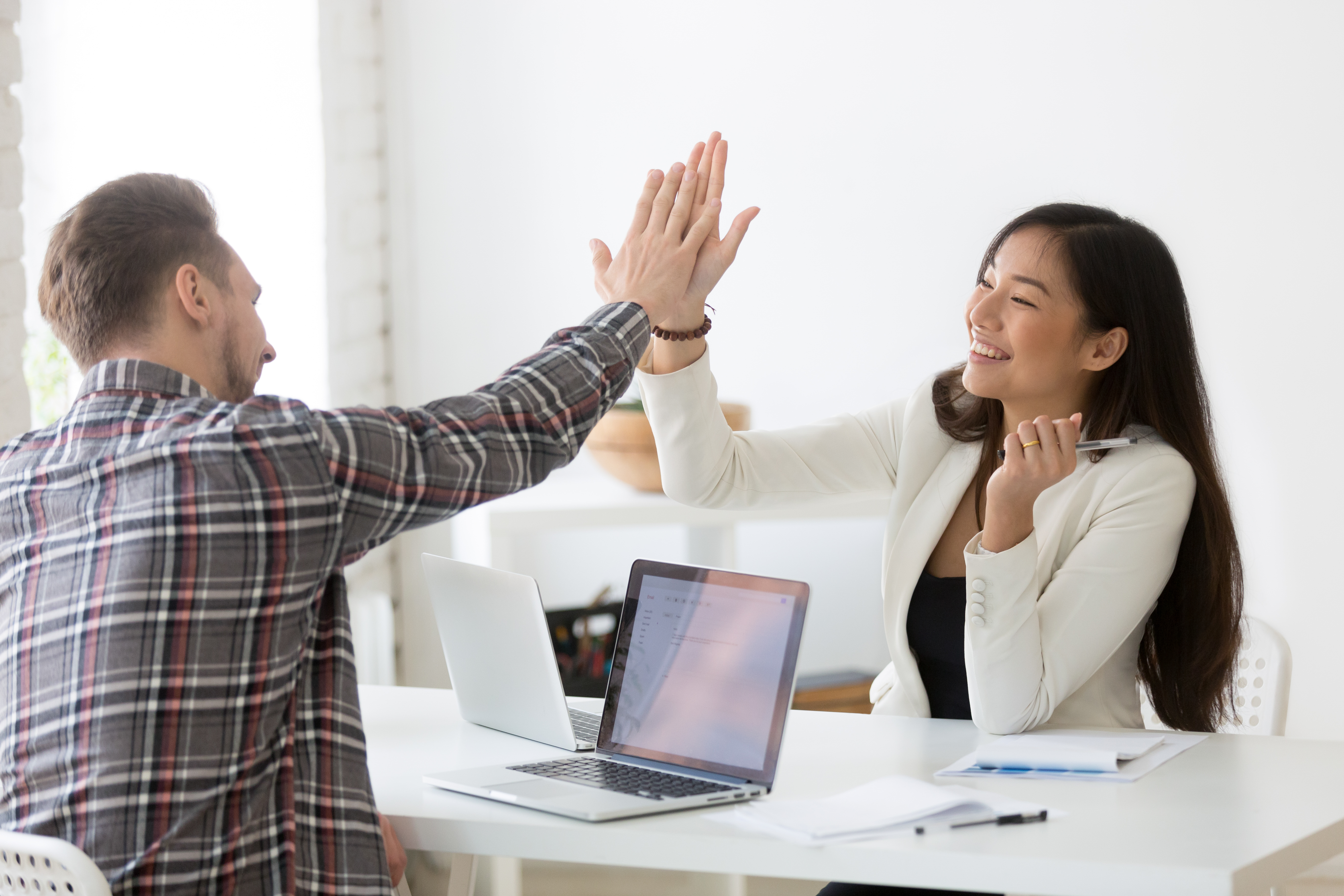 Young Asian And Caucasian Partners Giving High Five At Workplace
